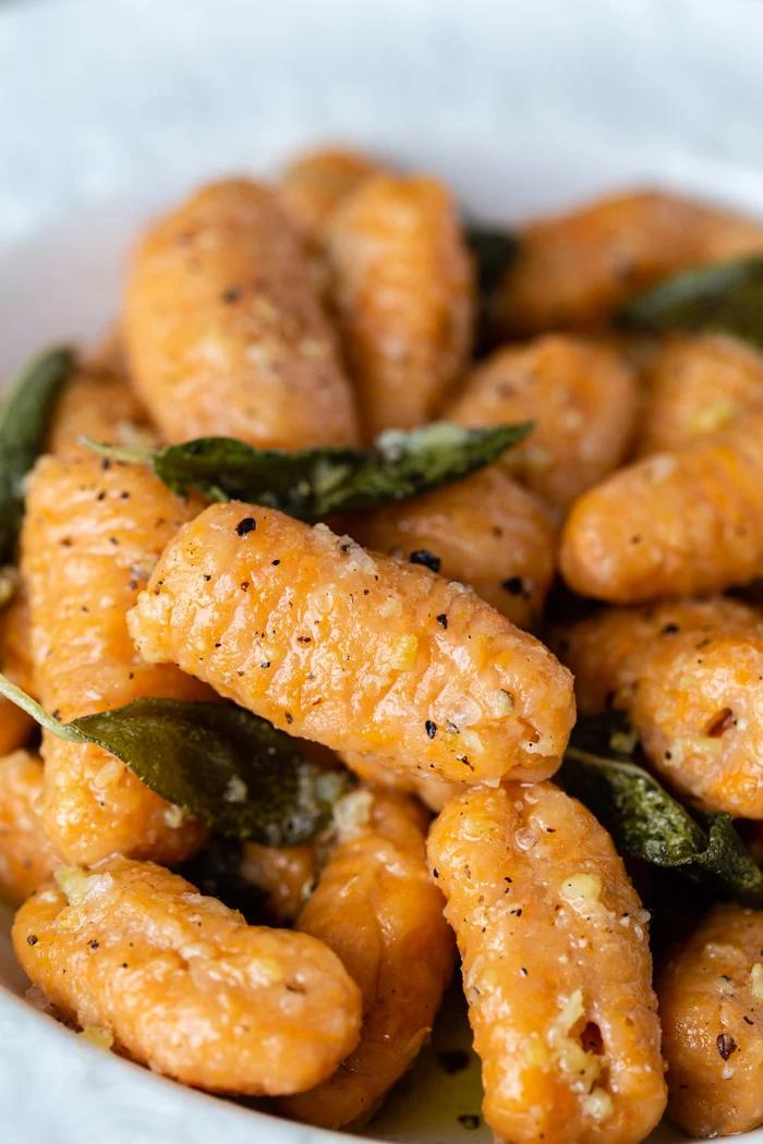 side shot of sweet potato gnocchi in a sage sauce. In a white bowl
