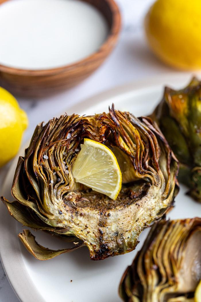 cookes and crispy artichokes with a small piece of lemon in the middle and white sauce in the background