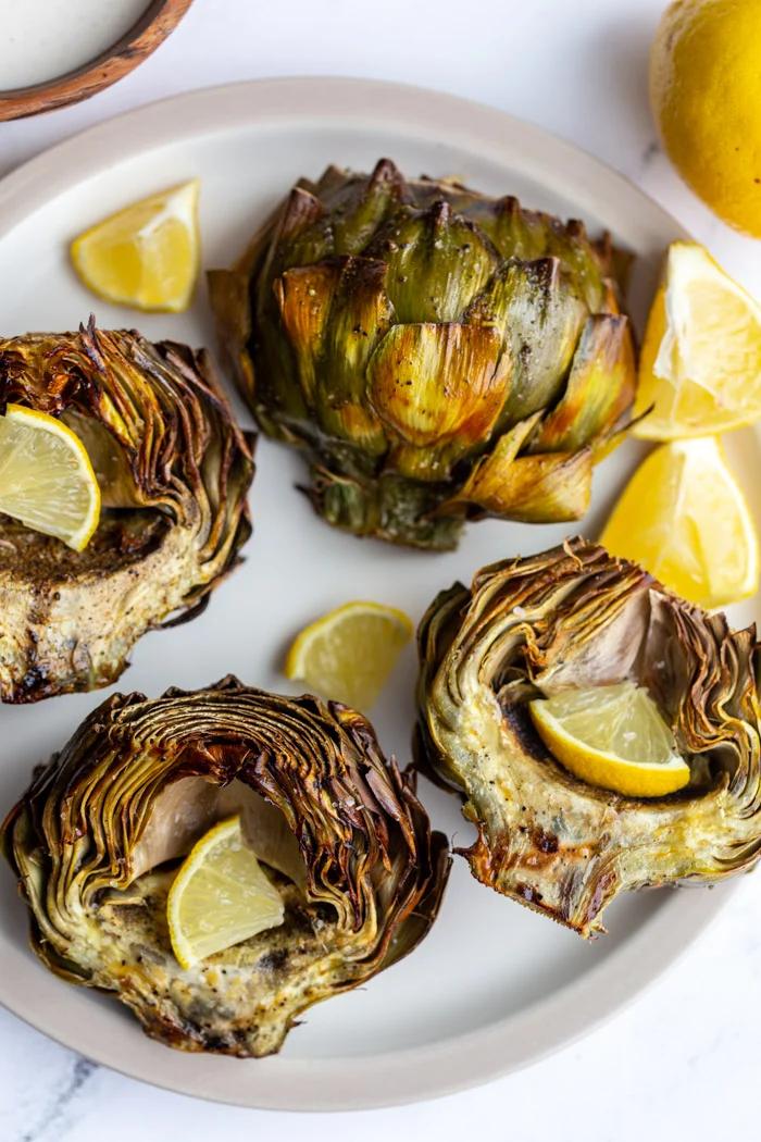 4 artichoke halves on a large plate. 1 is cut side down and the others are cut side up and all crispy with slices of lemon in the middle