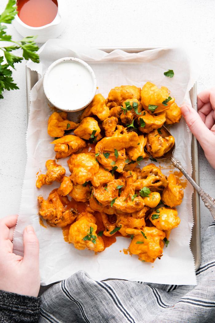 hands holding a tray of air fryer buffalo cauliflower with dipping sauce