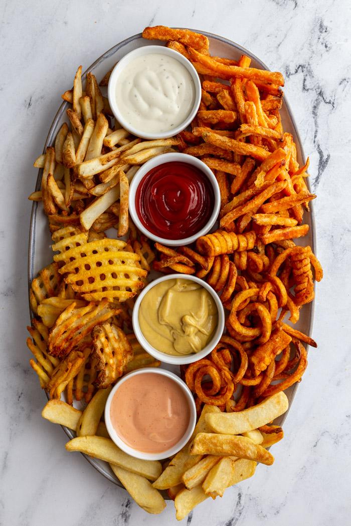 large tray of various kinds of french fries with 4 different flavors and colors of dips in small ramekins