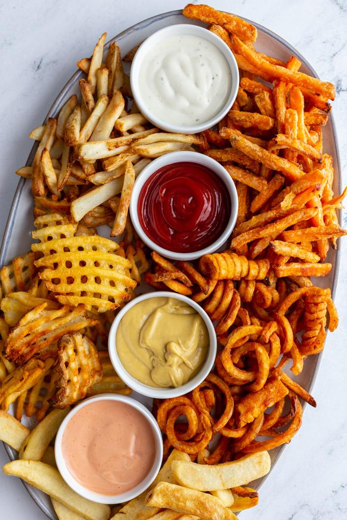 large tray of various kinds of french fries with 4 different flavors and colors of dips in small ramekins