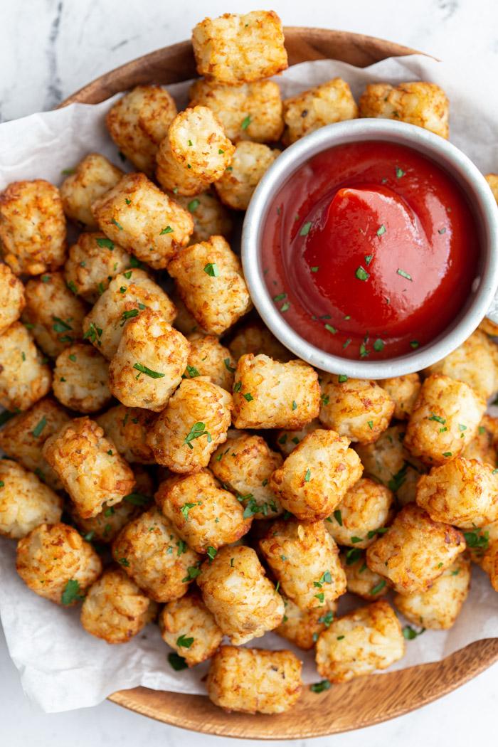 wood plate lined with parchment paper and topped with tater tots and a bowl of ketchup