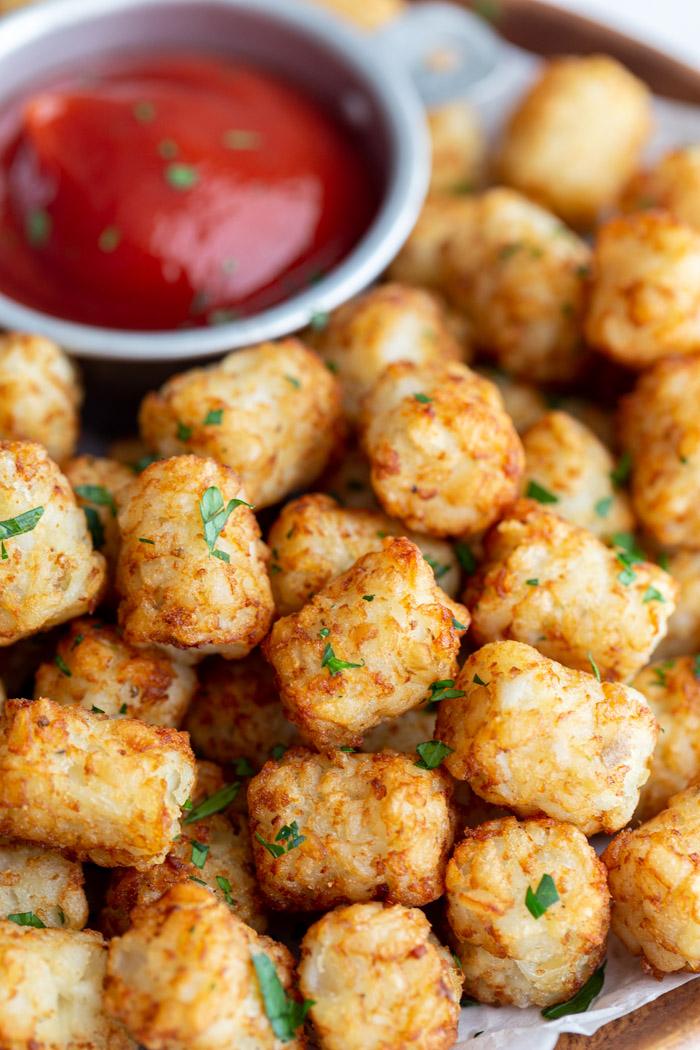 wood plate lined with parchment paper and topped with crispy tater tots and a bowl of ketchup