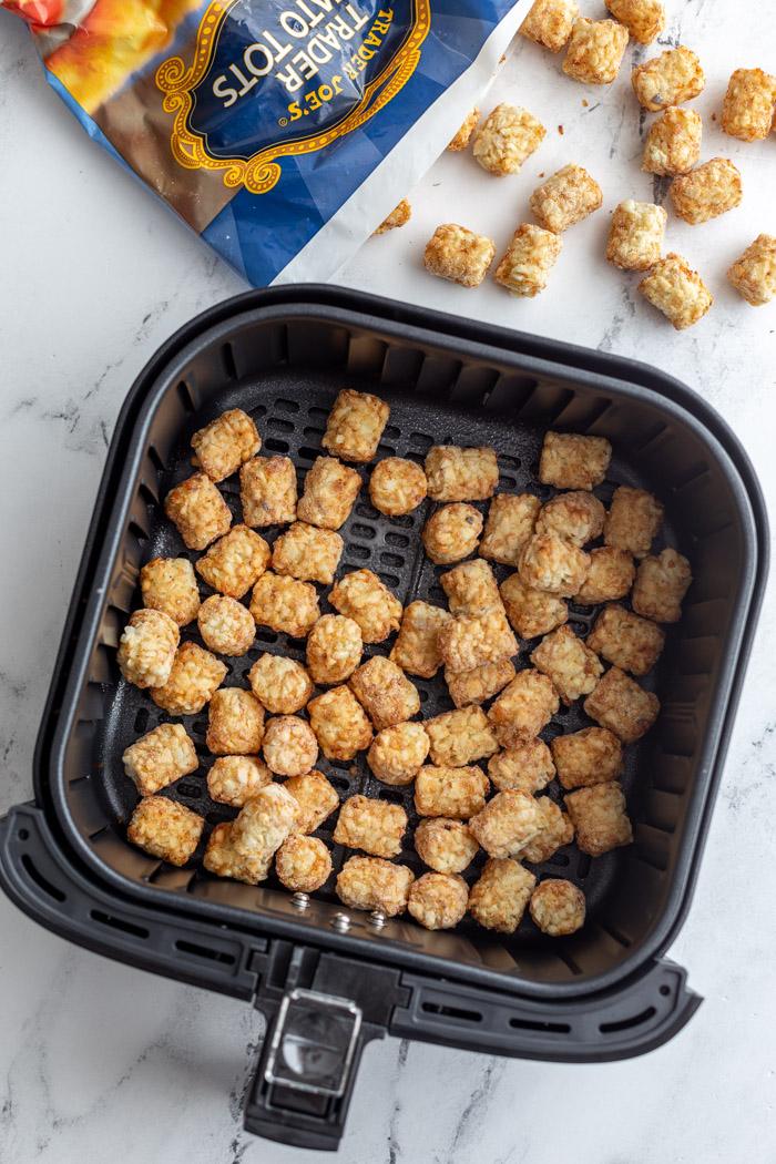 frozen tater tots in air fryer with the bag of tots in the top of the frame