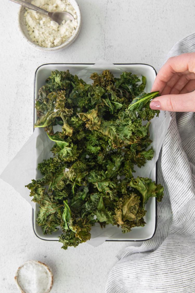 woman's hand grabbing a kale chip out of a serving tray