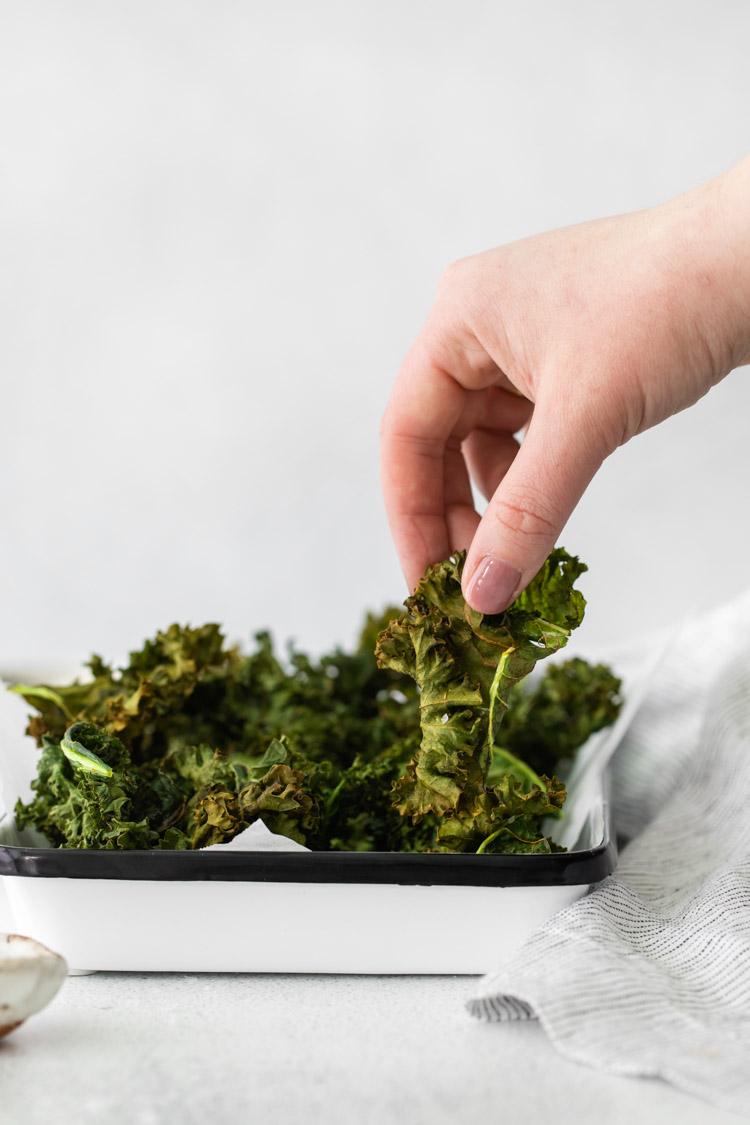 hand grabbing air fryer kale chips off of a serving plate