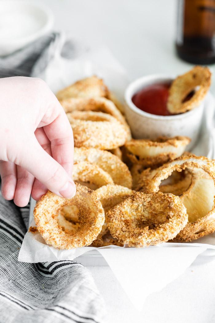 hand grabbing an onion ring off of a plate