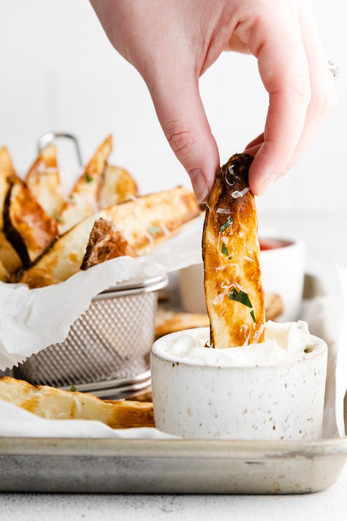 hand dipping a potato wedge in a small bowl of ranch
