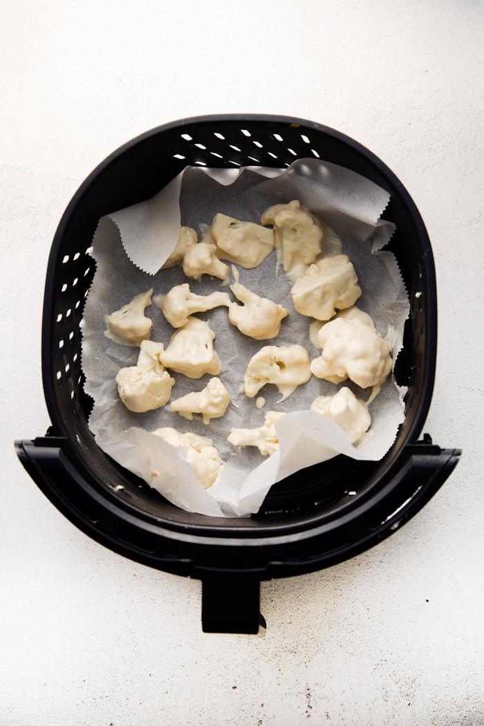 breaded cauliflower in an air fryer basket that's been lined with parchment paper