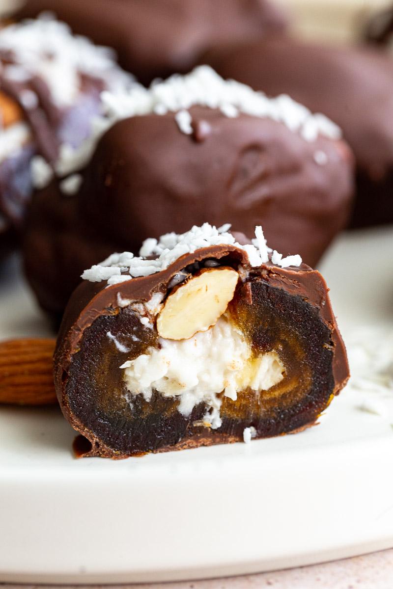 medjool dates stuffed with coconut and topped with an almond and meted chocolate- one is cut in half so you can see the inside