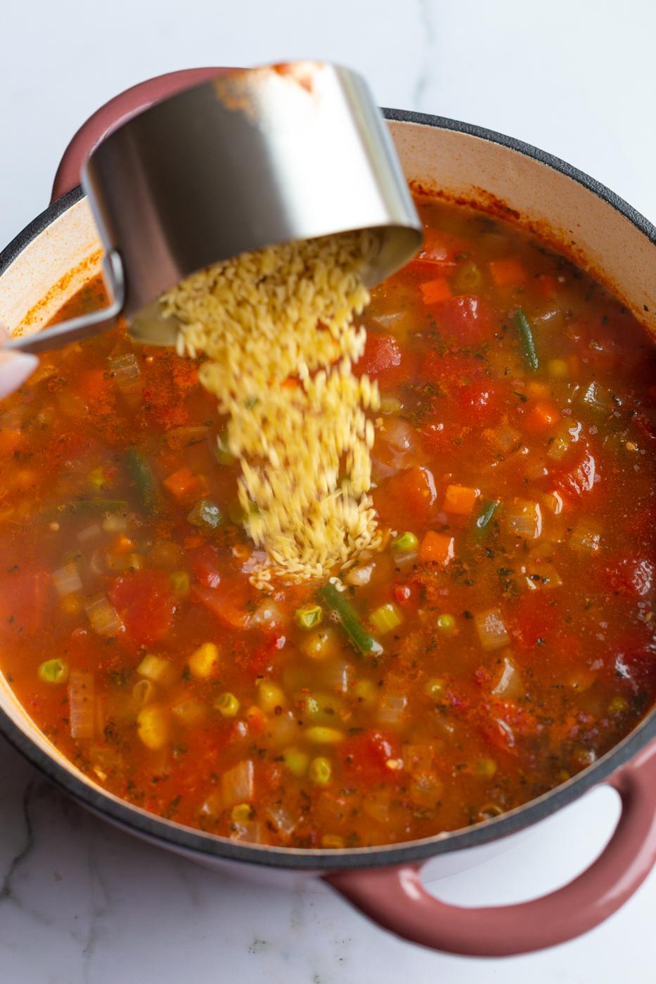 alphabet pasta being poured into a pot of soup