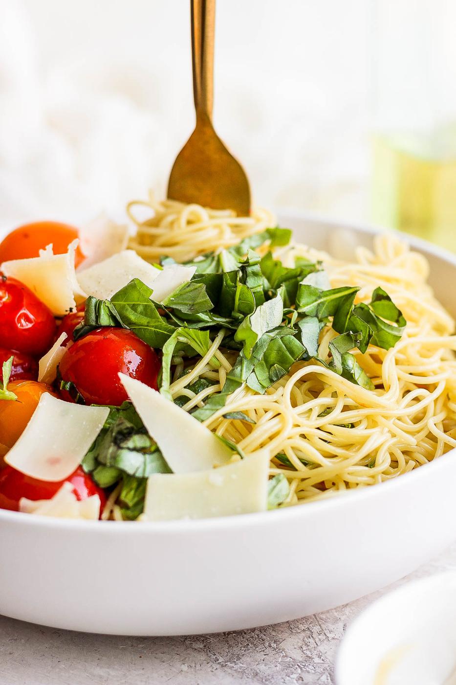 Pasta served in a white bowl with tomatoes and parmesan cheese.