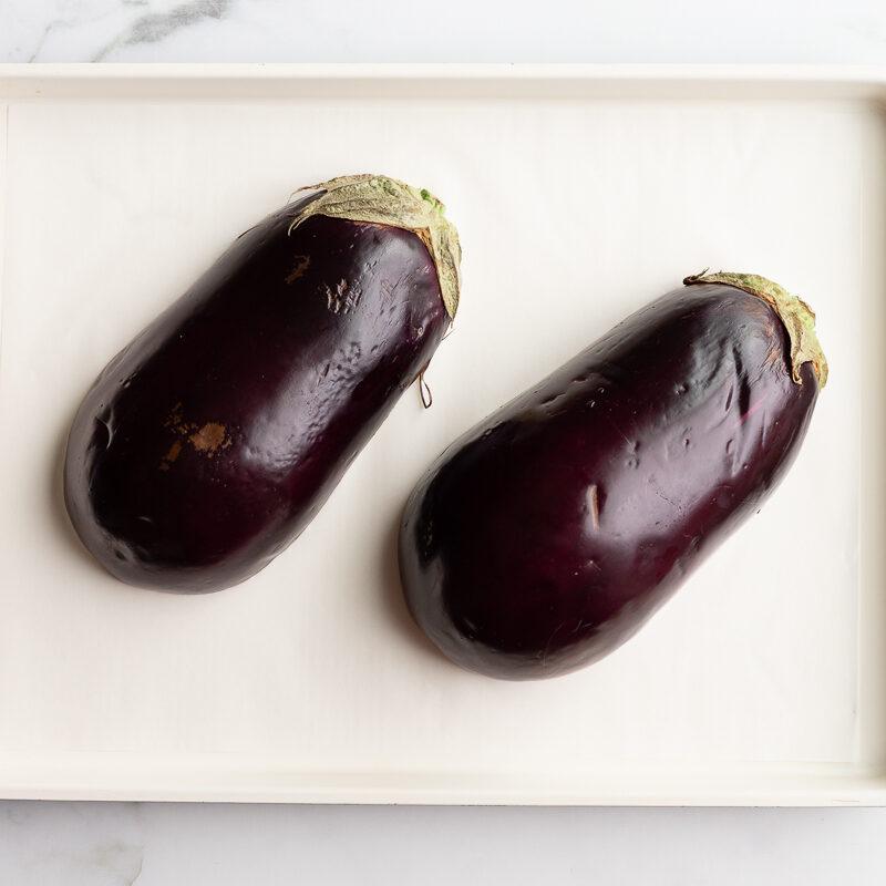 one eggplant halved lengthwise on a parchment-lined baking sheet before roasting