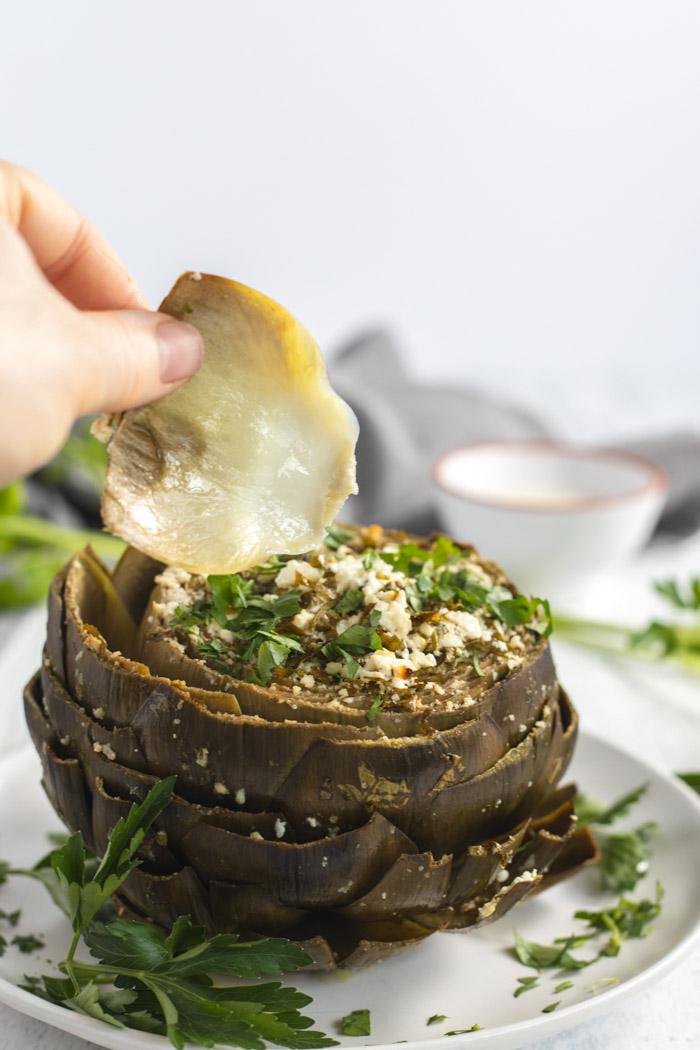 pulling a leaf off of a baked artichoke