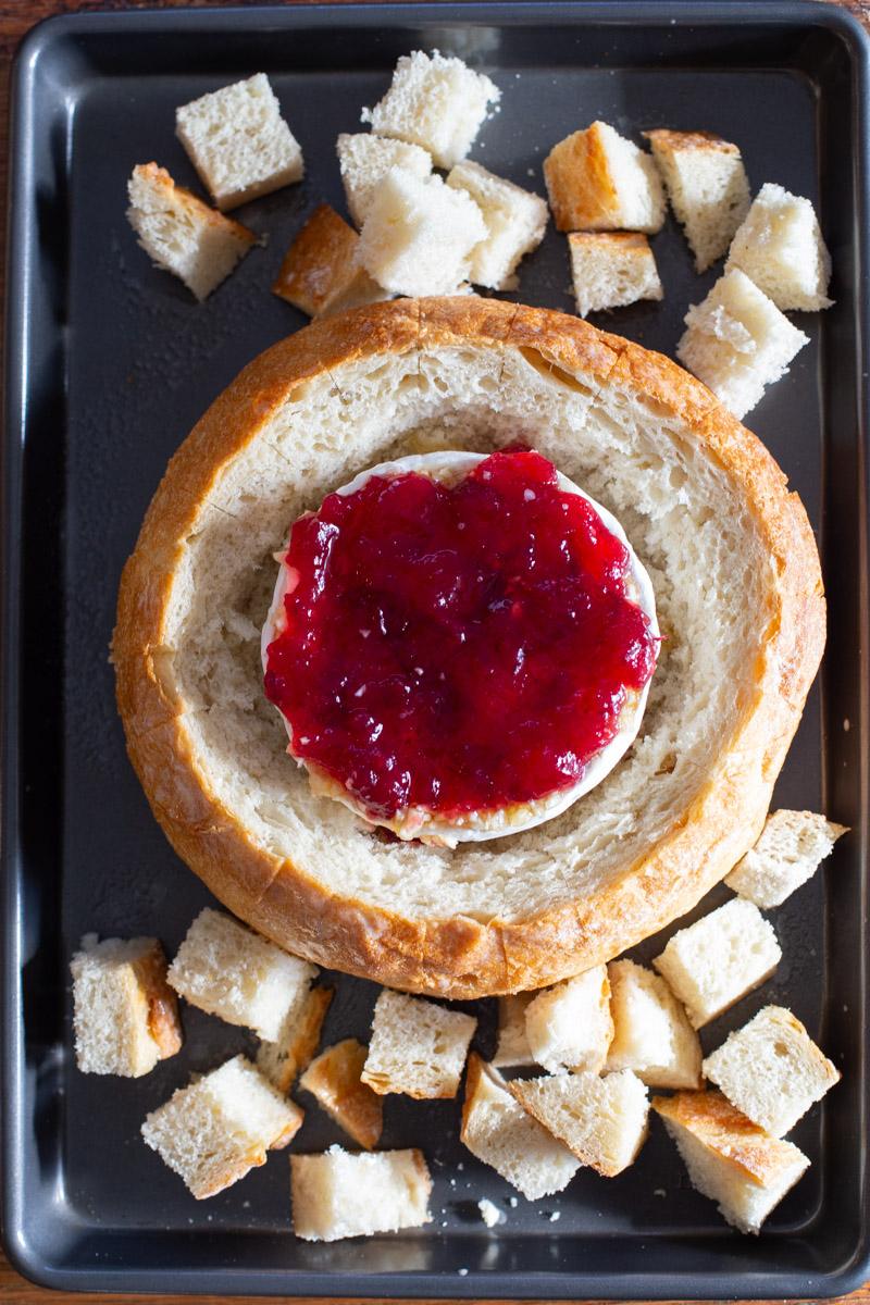 baked cranberry brie in a loaf of bread with more bread around it on the baking sheet
