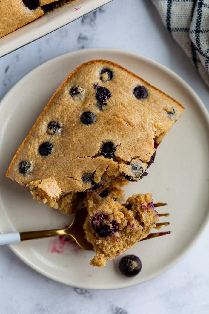 baked oatmeal on a plate with blueberries on top and a bite taken out by a fork