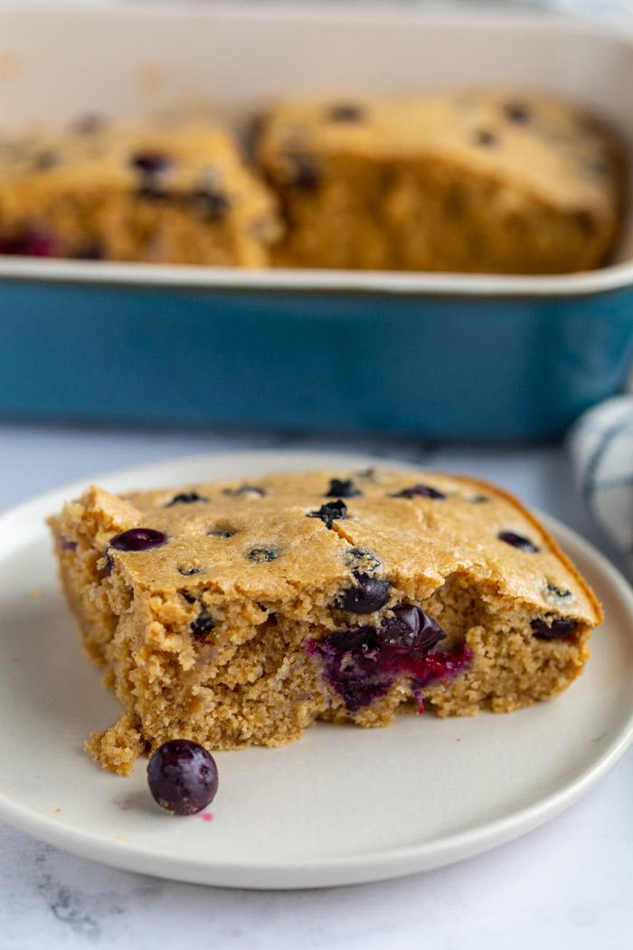 slice of baked oats in a plate with the casserole dish of the rest of the baked oats in the background