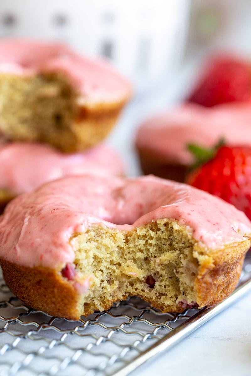 baked donuts topped with a pink strawberry glaze. big bite take out of the front donut