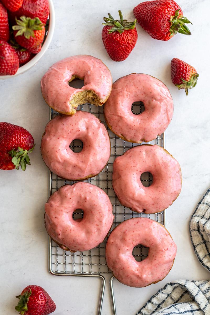 strawberry glazed donuts on a wire cooling rack with fresh strawberries around