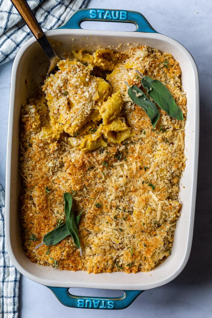teal colored casserole dish filled with baked vegan mac and cheese and fresh herbs