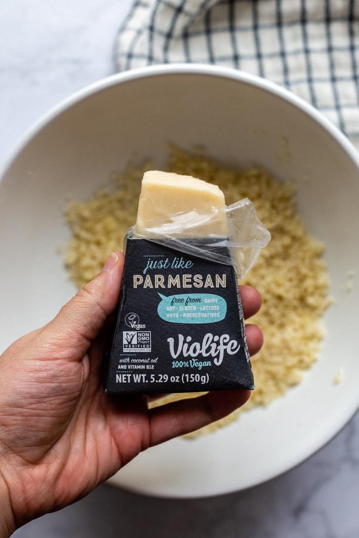 block of violife vegan parmesan cheese being held over a bowl of breadcrumbs