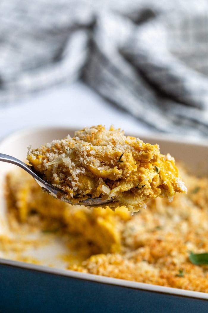 scoop of mac and cheese being pulled out of a casserole dish and topped with breadcrumbs