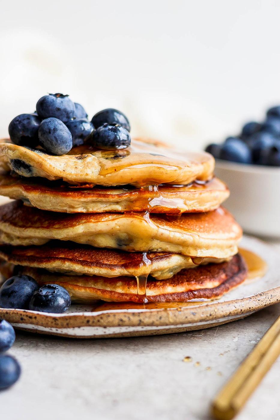 Stack of pancakes on a plate with blueberries and syrup.