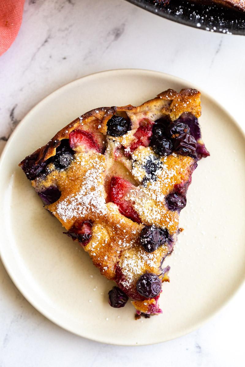 slice of blueberry and strawberry dutch baby dusted with powdered sugar