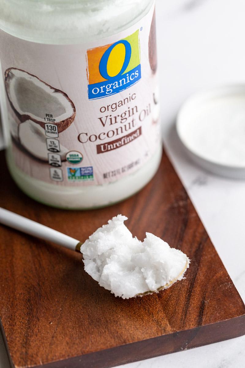 jar of coconut oil with a spoonful of coconut oil resting on a wood board