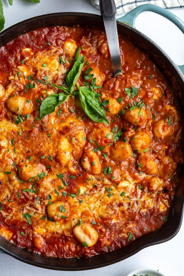 skillet with tomato sauce and gnocchi covered with cheese and garnished with fresh basil