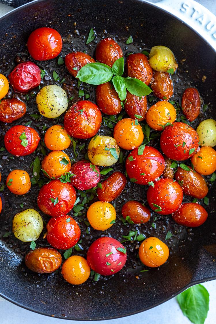 cherry tomatoes sautéing in a cast iron skillet