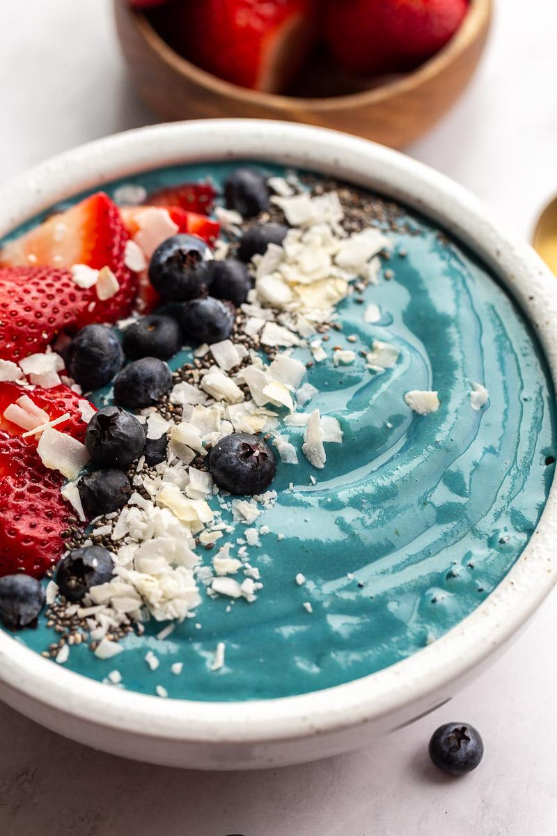 Blue smoothie bowl topped with berries and shredded coconut.