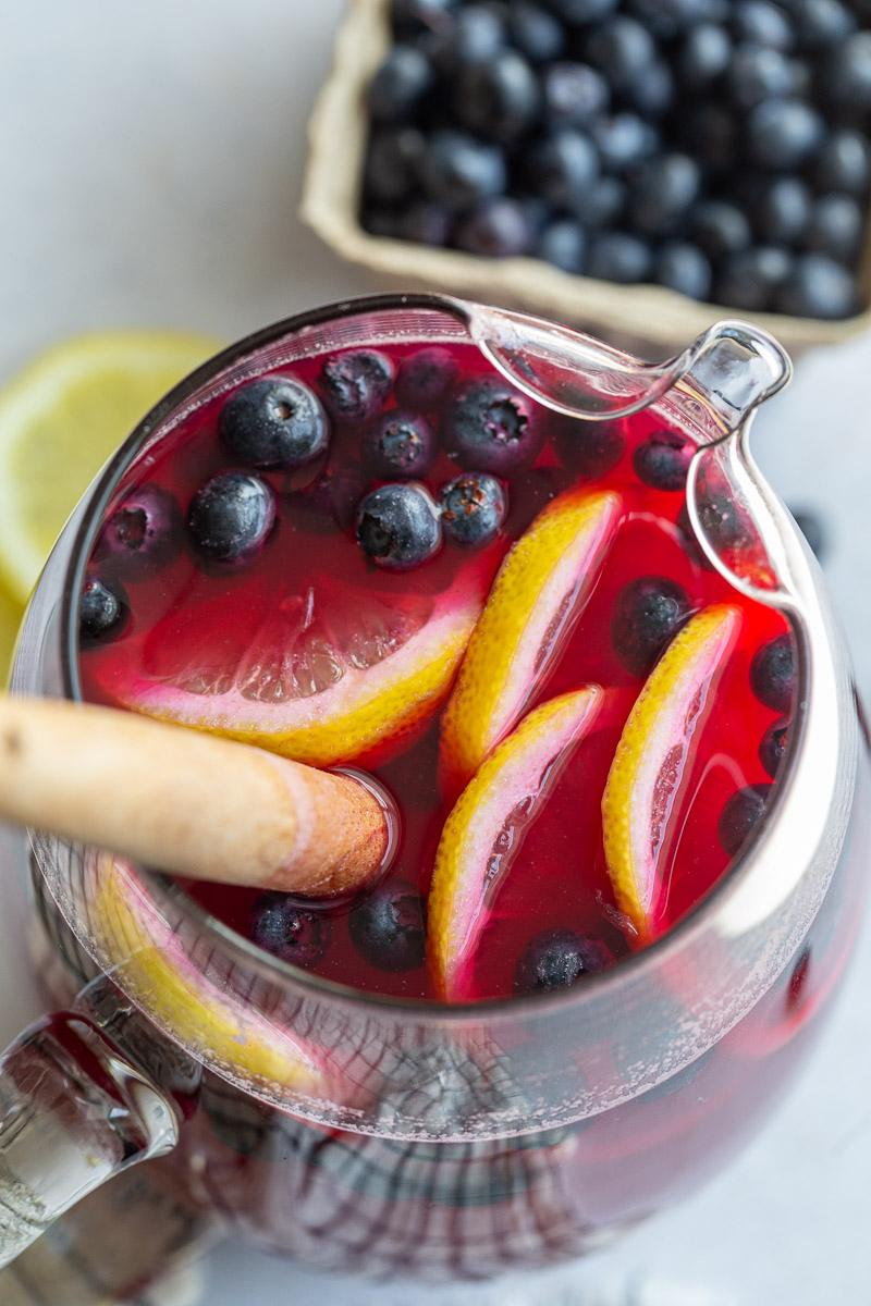 Overhead view of a bright pink drink garnished with fresh blueberries and lemon slices.