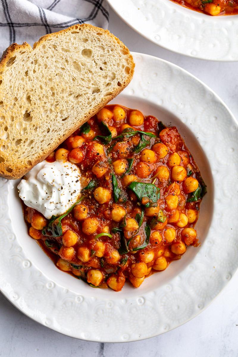 Bowl filled with chickpeas cooked in tomato sauce with spinach.