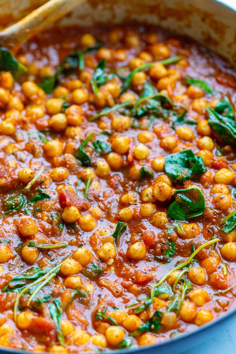 Stirring chickpeas with tomato sauce in a large pot.