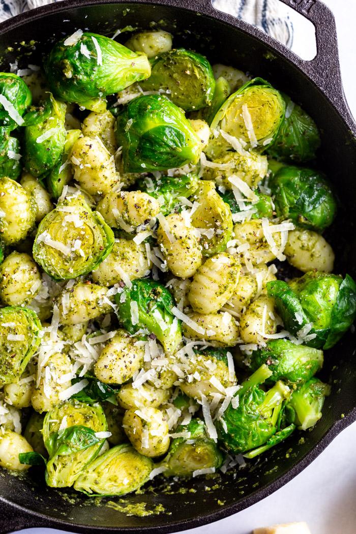 black cast iron skillet filled with gnocchi and brussels sprouts in a pesto sauce and topped with with fresh cheese