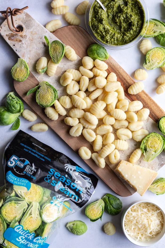 gnocchi on a wood board with brussels sprouts and pesto in the scene. a package of ocean mist speedy cook sprouts in the corner