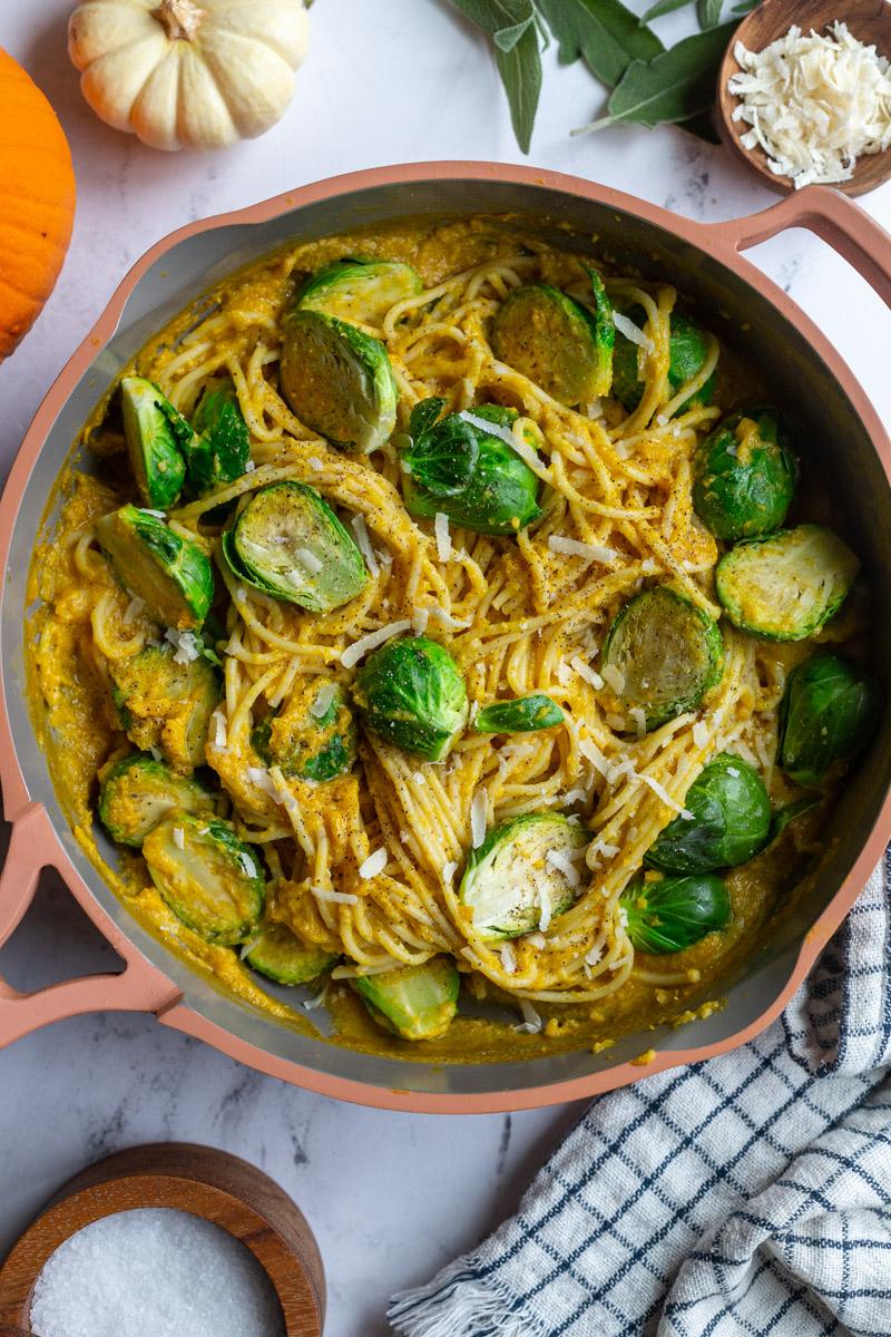 creamy pumpkin pasta spaghetti in a skillet with brussels on top and small pumpkins in the corner of the shot