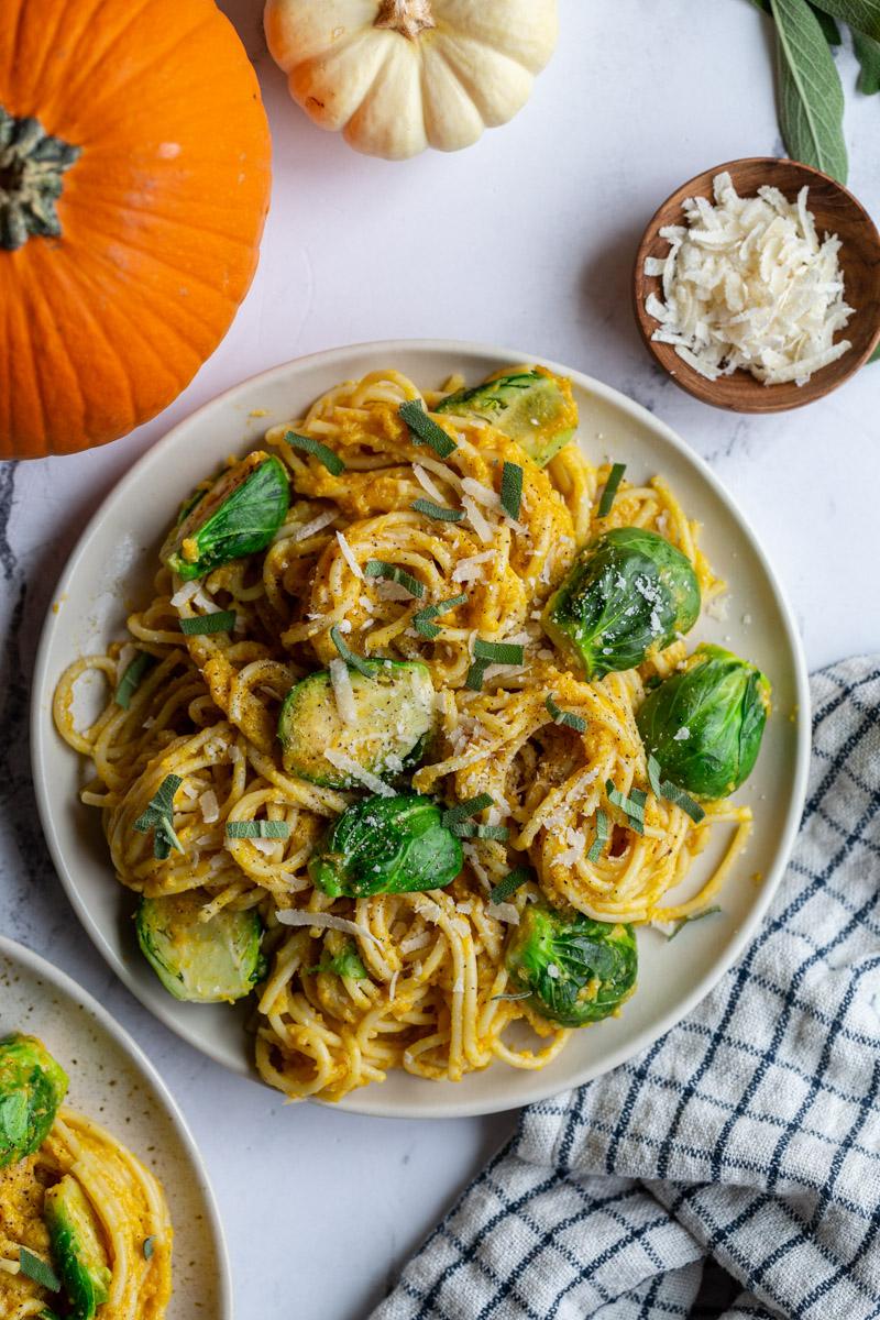 creamy pumpkin pasta spaghetti on a plate with brussels on top and small pumpkins in the corner of the shot