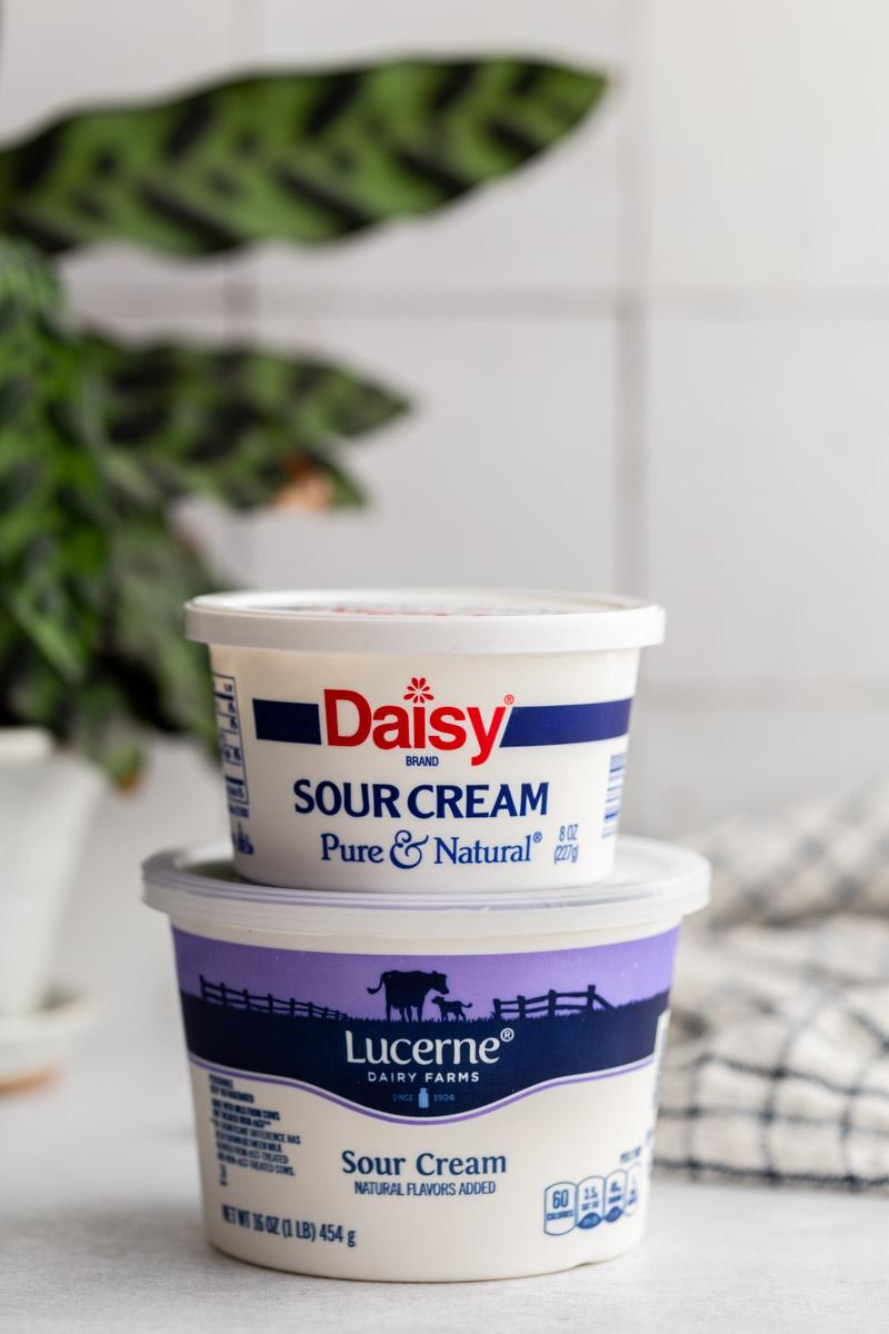 2 tubs of sour cream stacked on top of each other with a plant in the background