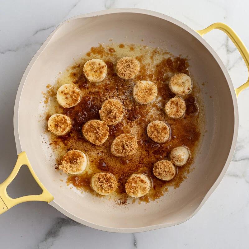 bananas and brown sugar in a yellow skillet to caramelize them