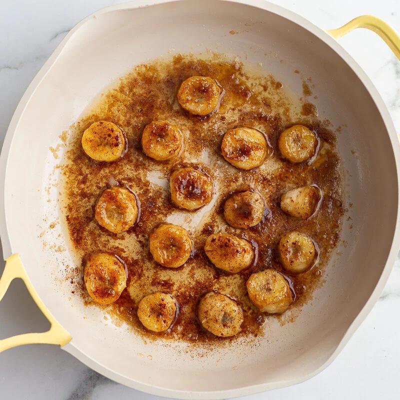 bananas and brown sugar cooking in a yellow skillet to caramelize them