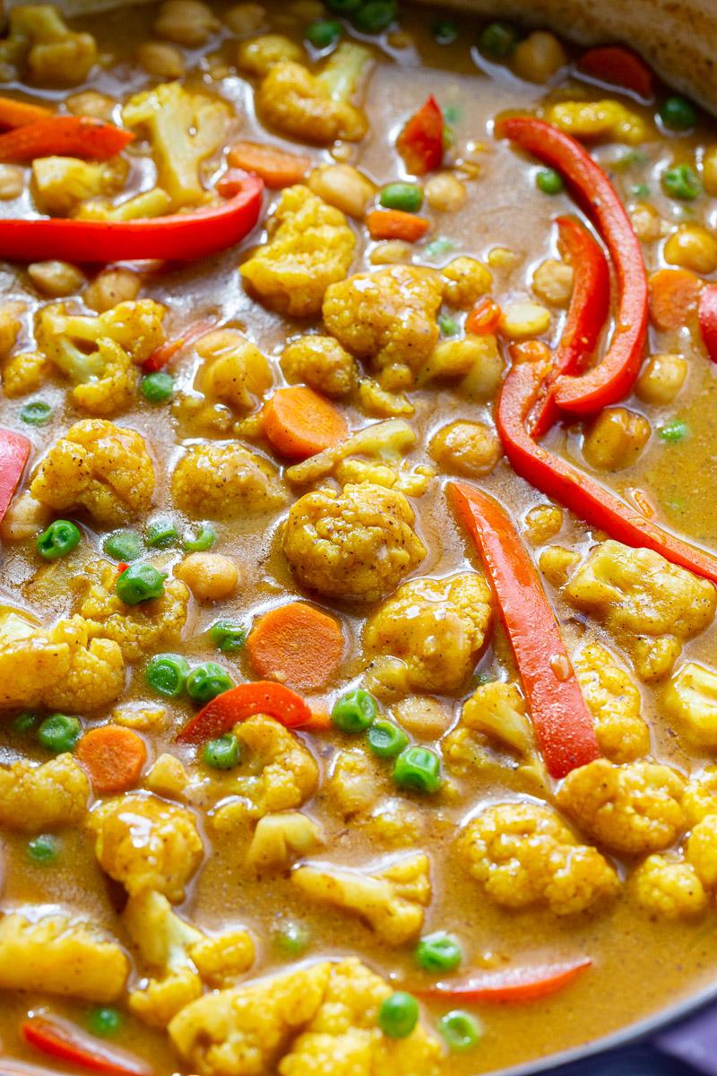 Cauliflower and veggies in a sauce cooking in a skillet.