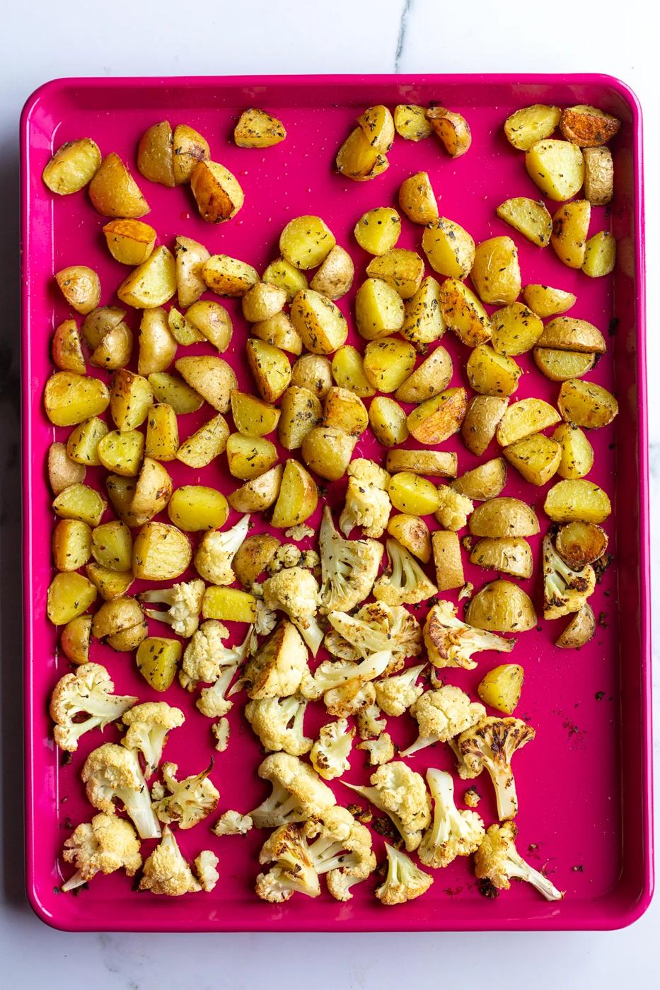 roasted baby potatoes and cauliflower on a red baking sheet