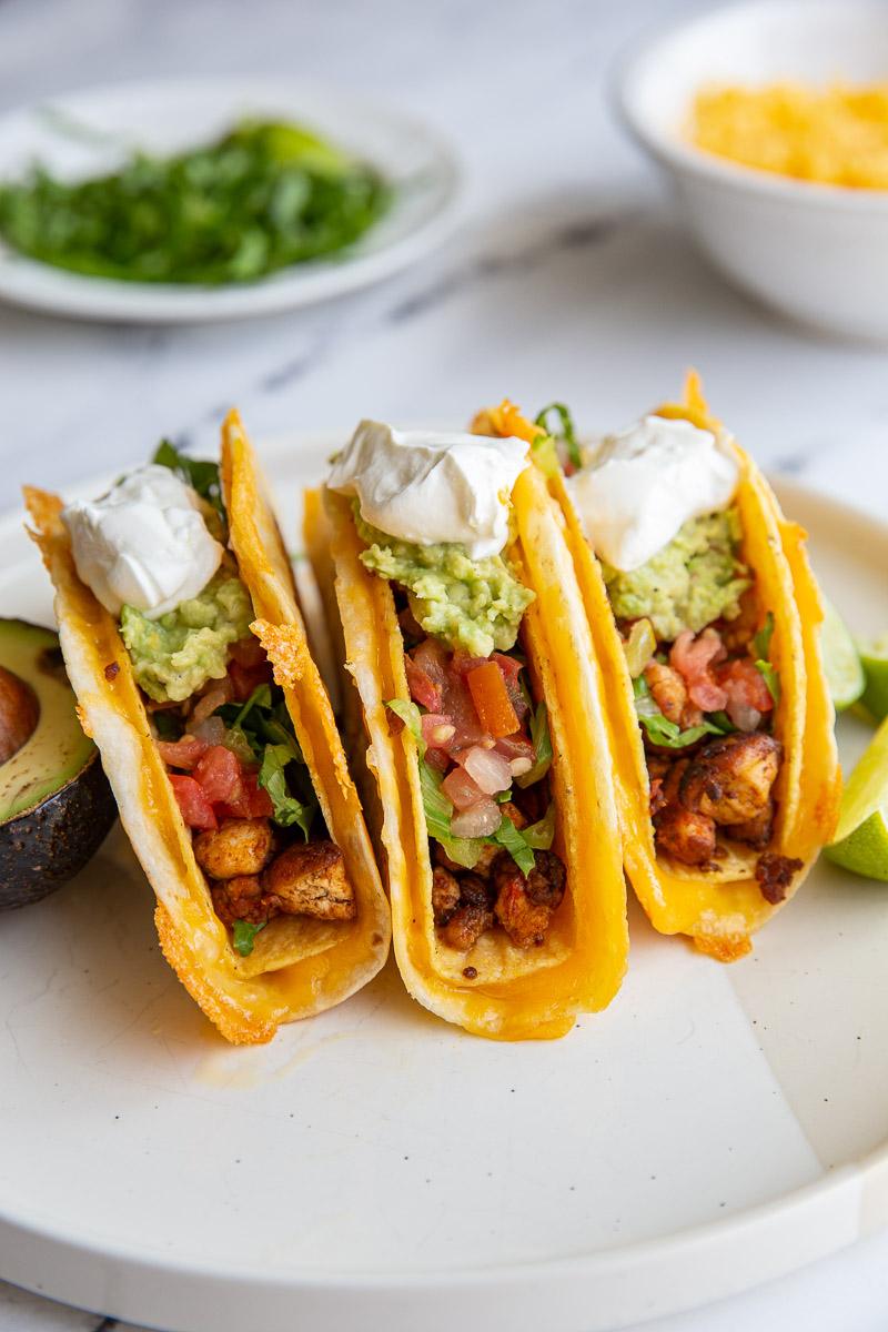 3 cheesy stuffed tacos topped with guacamole and sour cream on a plate
