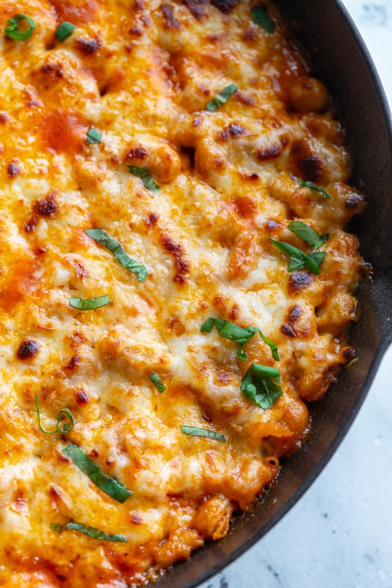 close up of a white bean tomato bake topped with lots of white cheese and fresh basil ribbons. In a white cast iron skillet