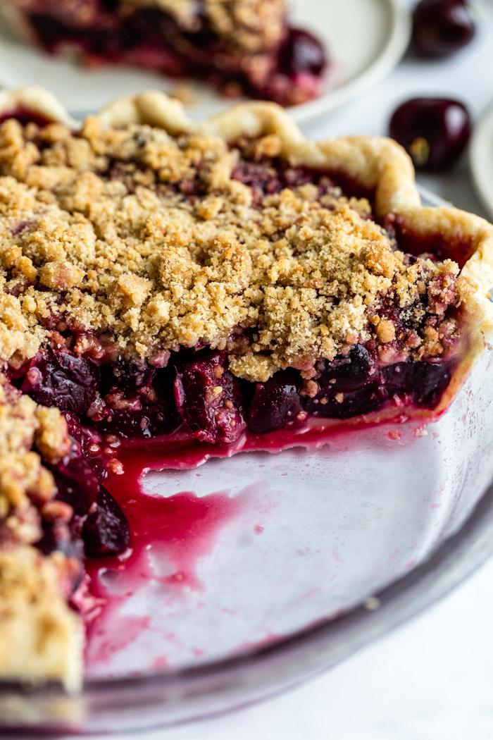 side shot of a cherry pie with a crumble topping. a slice is taken out and you can see the inside