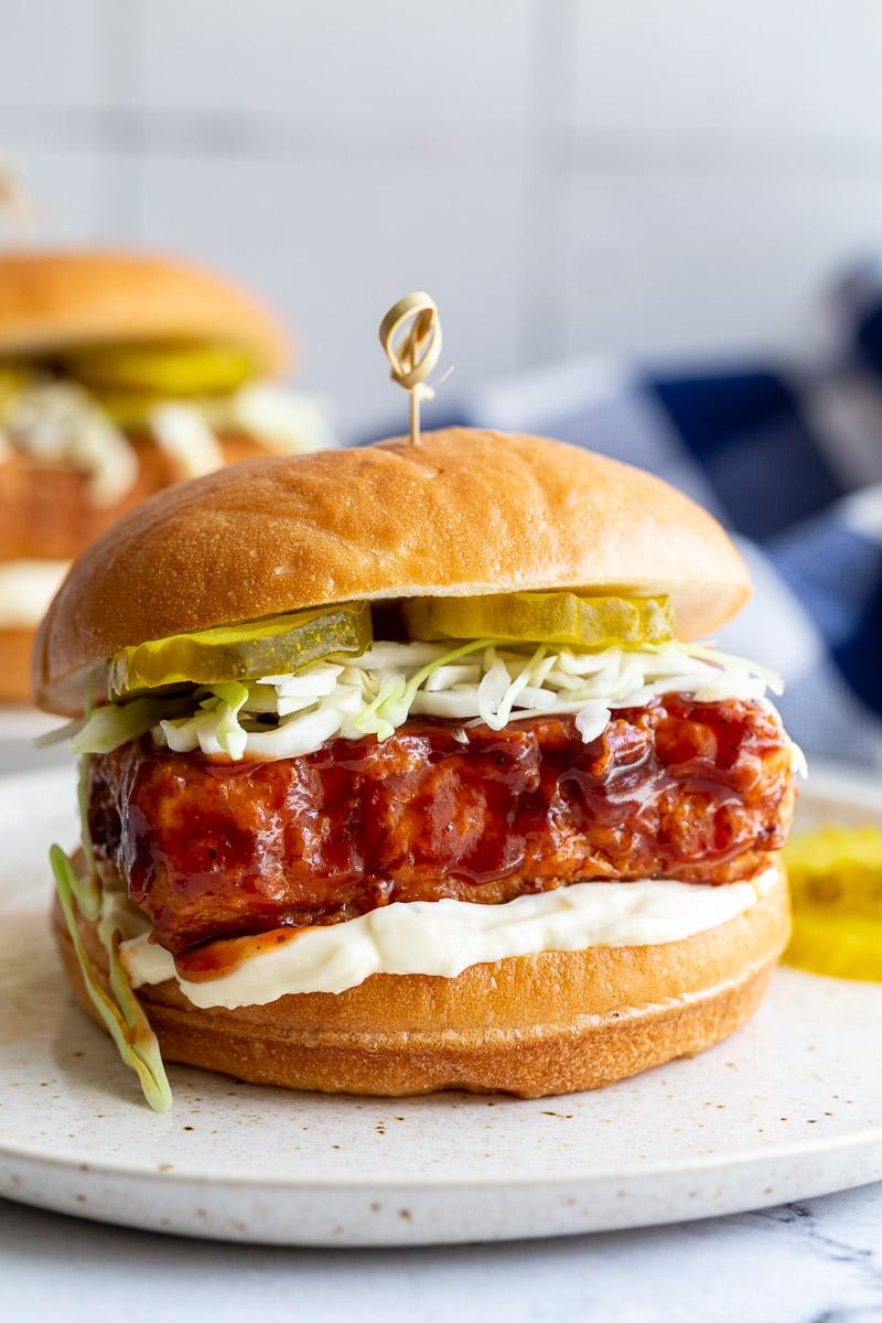 tofu "chicken" BBQ sandwich on a bun with mayo, cabbage and pickles and a toothpick in the center