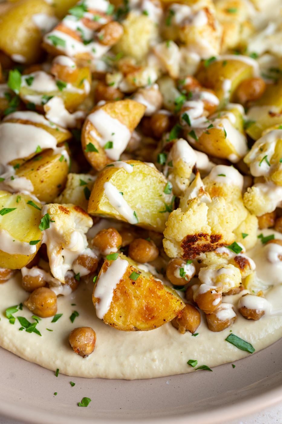 veggie bowl with roasted potato, chickpeas and cauliflower on a bed of creamy hummus and drizzled with a white tahini sauce